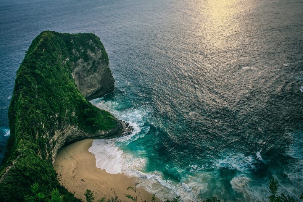 A breathtaking panoramic view of a serene beach and turquoise ocean, captured from a high cliff overlooking the coastline.