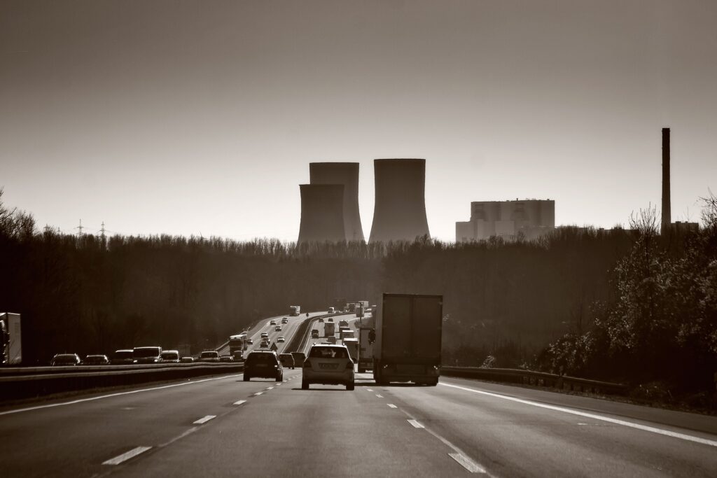 Cars passing by a large factory with visible chimneys and industrial activity.