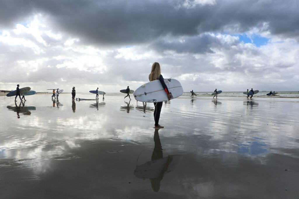 A female surfer standing confidently with a group of surfers in the background.