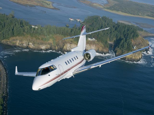 A sleek private jet flying diagonally through a clear blue sky.