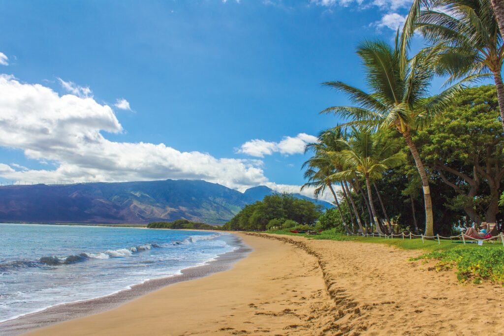 A serene beach with soft, light brown sand gently sloping toward the turquoise ocean waves.